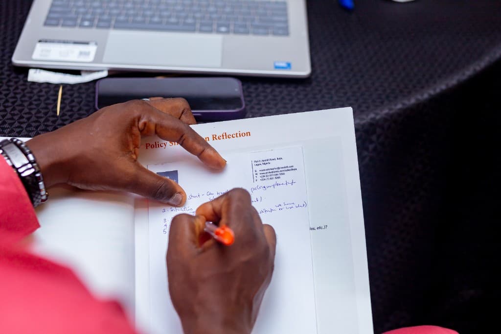 Close-up of hands annotating a printed policy reflection worksheet beside a laptop