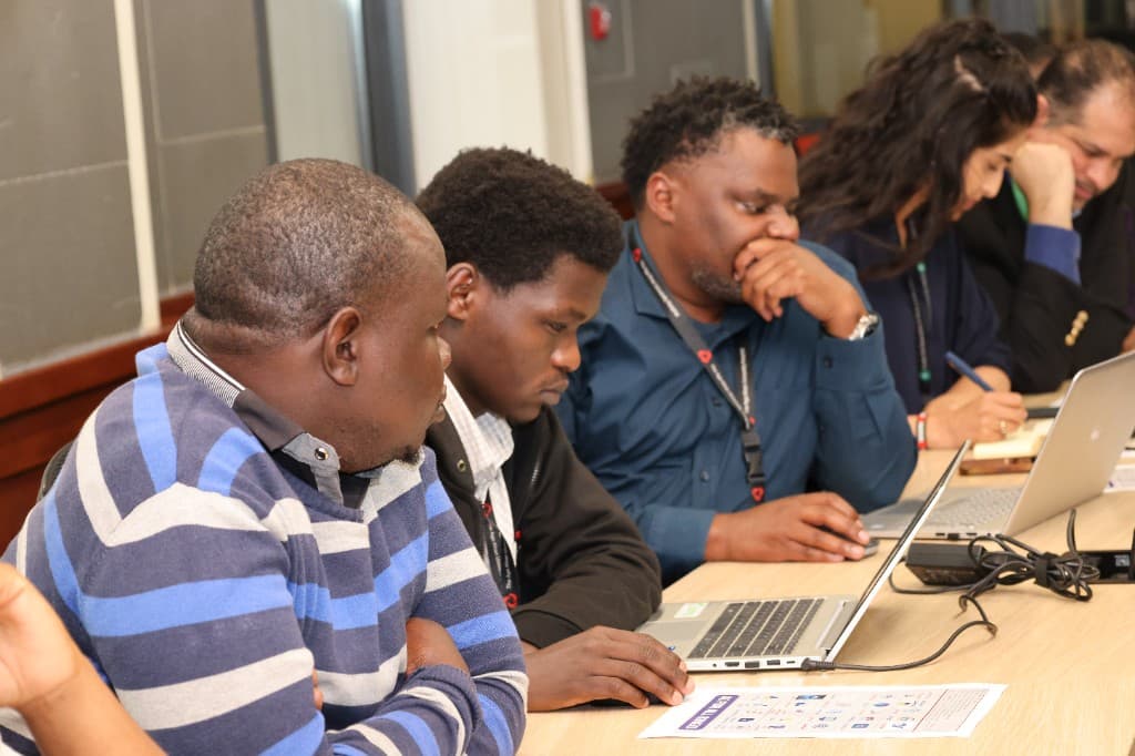 Professionals seated at a long table working on laptops during a collaborative workshop
